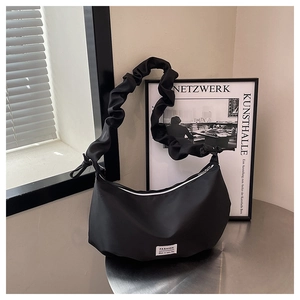 Detail of black crescent hobo bag with unique ruched cloud strap on metal table