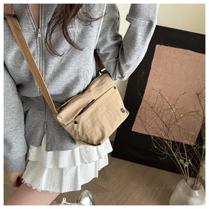 Detailed view of a khaki nylon crossbody bag styled in a minimalist indoor setting