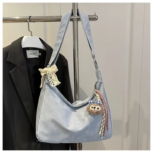 Détail du sac hobo bleu clair au fini mat avec un nœud en dentelle et un pendentif