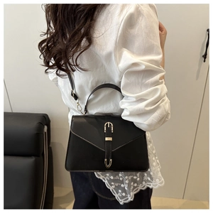 Photo d'un sac bandoulière en cuir noir avec fermoir doré porté par un mannequin en mode