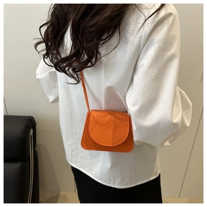 Detail of orange mini crossbody bag with pebble leather texture worn on white shirt