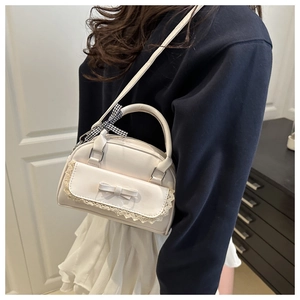 Close-up of a cream shell-shaped shoulder bag with lace trim and bow charm detail