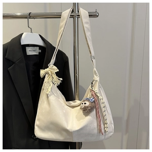 Détail du sac croissant blanc avec nœud en dentelle et breloque singe sur blazer noir