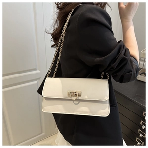 Detail of a white leather baguette bag with a gold metal clasp and chain strap on a model