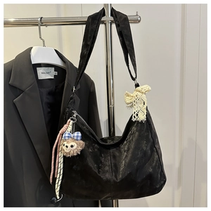 Détail d'un grand sac hobo noir à bandoulière avec nœud en dentelle et breloque peluche