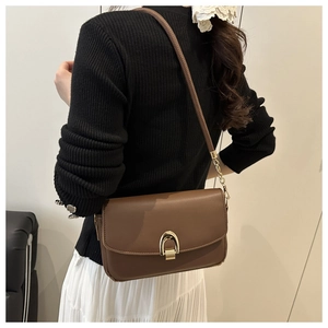 Close-up of brown leather shoulder bag with gold horseshoe buckle on elegant female model