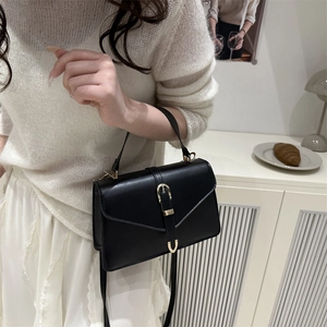 Sac bandoulière noir minimaliste avec boucle dorée porté par un mannequin en blanc