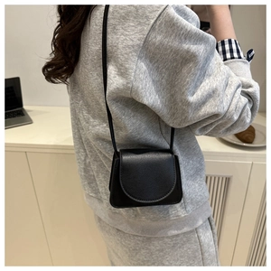 Detail of a black mini crossbody bag with litchi grain texture and curved flap closure