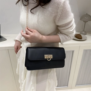 Sac baguette noir minimaliste avec fermoir doré et bandoulière chaîne porté par femme