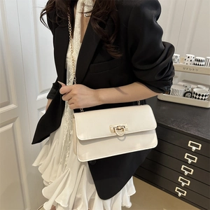 Sac baguette blanc crème avec chaîne dorée porté par une femme en blazer noir élégant