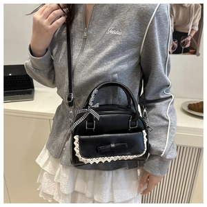 Close-up of black shell bag with white lace trim and adjustable leather shoulder strap