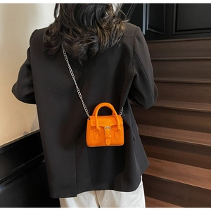 Détail du micro sac orange vif avec bandoulière chaîne argentée sur blazer noir