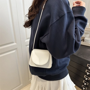 Chic white mini crossbody bag with litchi texture shown on model in warm indoor setting