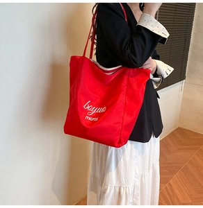 Detail of red large capacity nylon tote bag with white lettering and slim shoulder strap