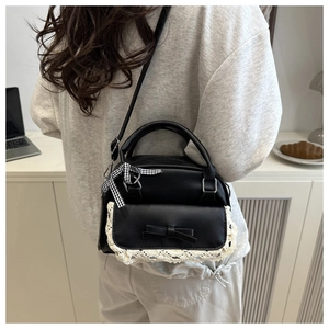 Detail of black shell bag with lace trim, leather bow, and checkered ribbon charm
