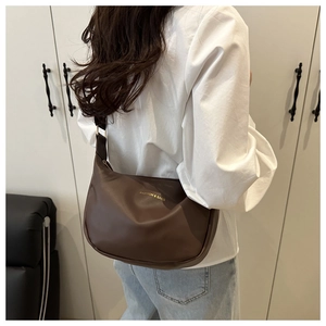 Détail du sac à bandoulière en cuir mat marron foncé avec texte doré sur le mannequin