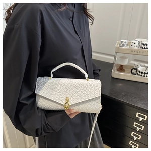 Close-up of white croc-embossed handbag featuring unique gold treble clef musical note clasp