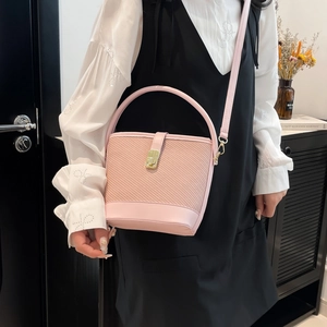 Pink woven bucket bag with leather base and gold buckle on a model in home setting