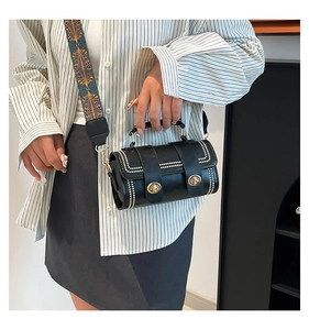 Detail of black cylinder bag featuring gold twist locks, white rivets and wide ethnic strap