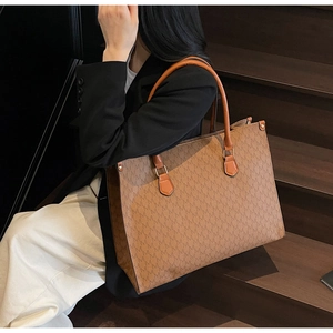 Detail of a brown tote bag with M-letter logo pattern carried by a model in a suit