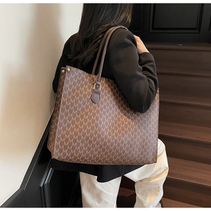 Gros plan sur le motif de lettres M et l'anse en cuir de ce grand sac cabas