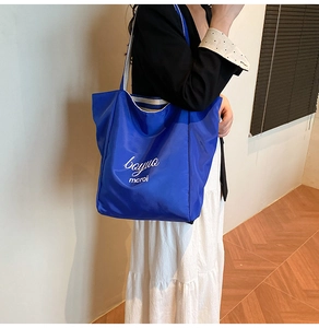 Detail of blue nylon tote bag with white letter print and striped woven handles