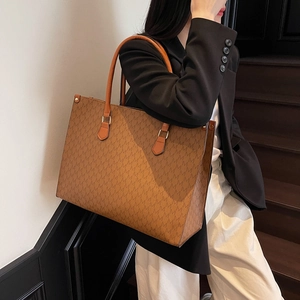 Brown leather tote bag with M-letter monogram print carried by model on stairs