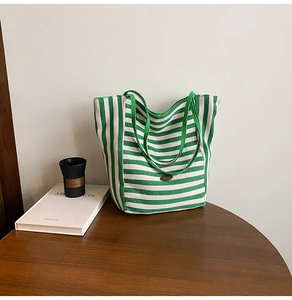 Close-up of green and white striped canvas tote bag with retro oval metal logo on wooden table