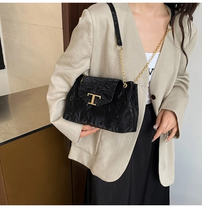 Dettaglio borsa a tracolla nera a pieghe con logo T dorato su un blazer beige elegante