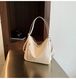 Detail of a creamy white shoulder bag with vertical zipper and adjustable strap on desk