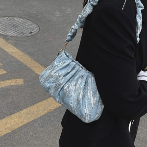 Blue sequined shoulder bag with ruched strap worn by a model in a street setting