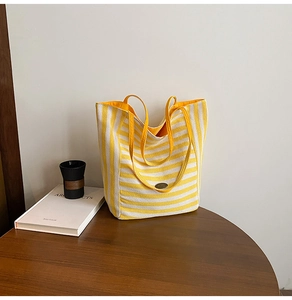 Detail of yellow and white striped canvas tote bag with woven handles on a wooden table