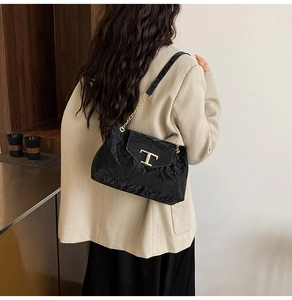 Dettaglio della borsa a spalla nera a pieghe con chiusura a T dorata su blazer beige