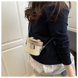 Detail of a mini beige woven bucket bag with khaki leather handles and a silver chain strap