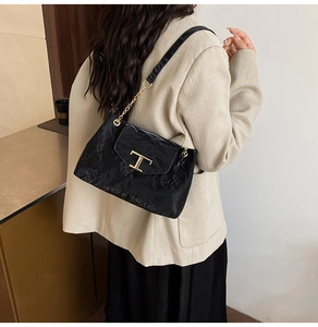 Dettaglio borsa in pelle nera a pieghe con chiusura a T dorata su blazer beige