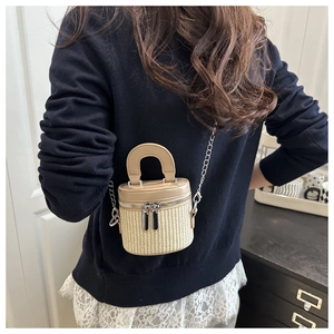Detail of a woven bucket bag featuring khaki leather handles and a silver chain strap