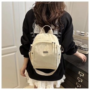 Detail of beige wrinkled nylon backpack showing side pocket and metal logo plate