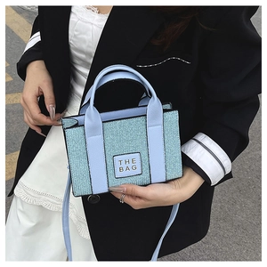 Detail of light blue mini tote with shiny fabric texture and THE BAG square logo patch