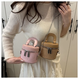 Detail of mini bucket bag with woven straw base and leather top featuring a metal chain strap