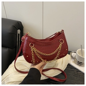 Close-up of burgundy crocodile pattern crescent bag with layered gold chain and rivets