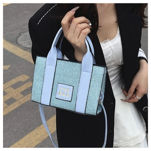 Detail of light blue woven tote bag with THE BAG leather patch and adjustable strap