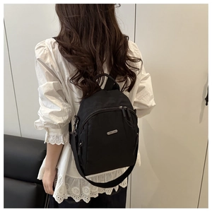 Detail of a black nylon commuter backpack showing the metal logo and outer zipper pocket