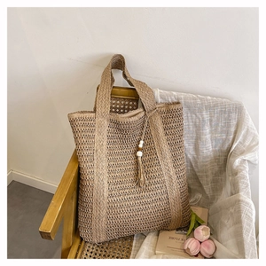 Detail of straw woven tote bag featuring natural texture and wooden bead tassels on a chair