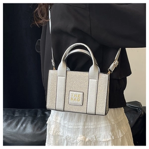 Detailed close-up of a silver metallic tote bag with The Bag leather patch and golden hardware