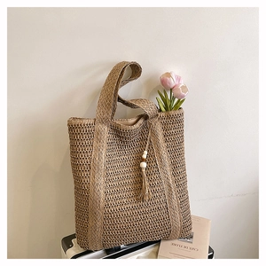 Detailed close-up of woven straw tote bag featuring bohemian tassels and wood beads