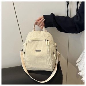 Detail of cream nylon backpack with metallic branding and long zipper pulls