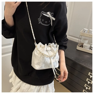 Sac seau brodé en dentelle avec anse en perles et chaîne dorée porté par un mannequin