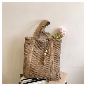 Detail of woven straw tote bag with beaded tassel charm and textured mesh pattern