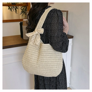 Detail of beige woven tote bag featuring a decorative bow knot on the shoulder strap