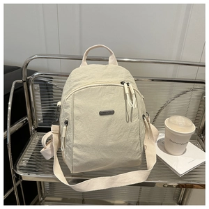 Detail of metal JING PIN logo and textured nylon fabric on beige women backpack